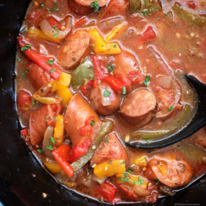 overhead shot of cooked sausage, bell pepper & onions in a black slow cooker