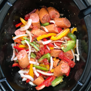 overhead shot of uncooked sausage, bell pepper & onions in a black slow cooker