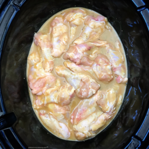 overhead shot of uncooked honey mustard chicken wings in a black slow cooker