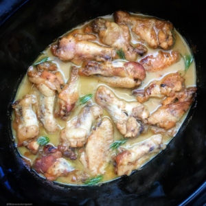 overhead shot of cooked honey mustard chicken wings in a black slow cooker