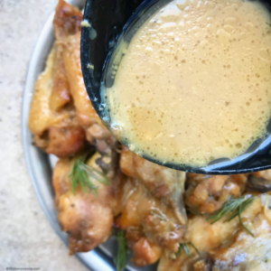 overhead shot of cooked honey mustard chicken wings on a white plate with sauce being poured on top