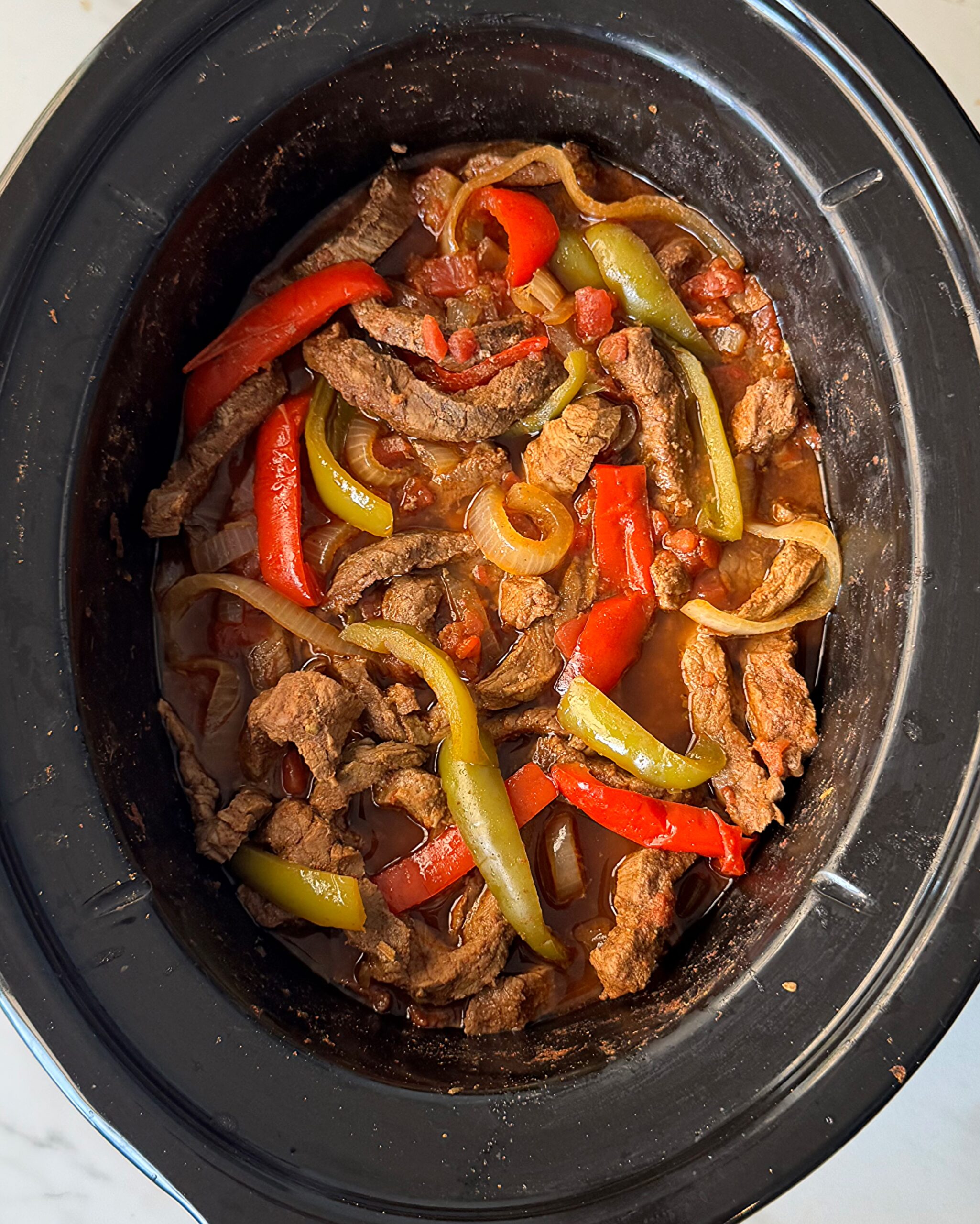 overhead shot of cooked steak fajitas in a black slow cooker