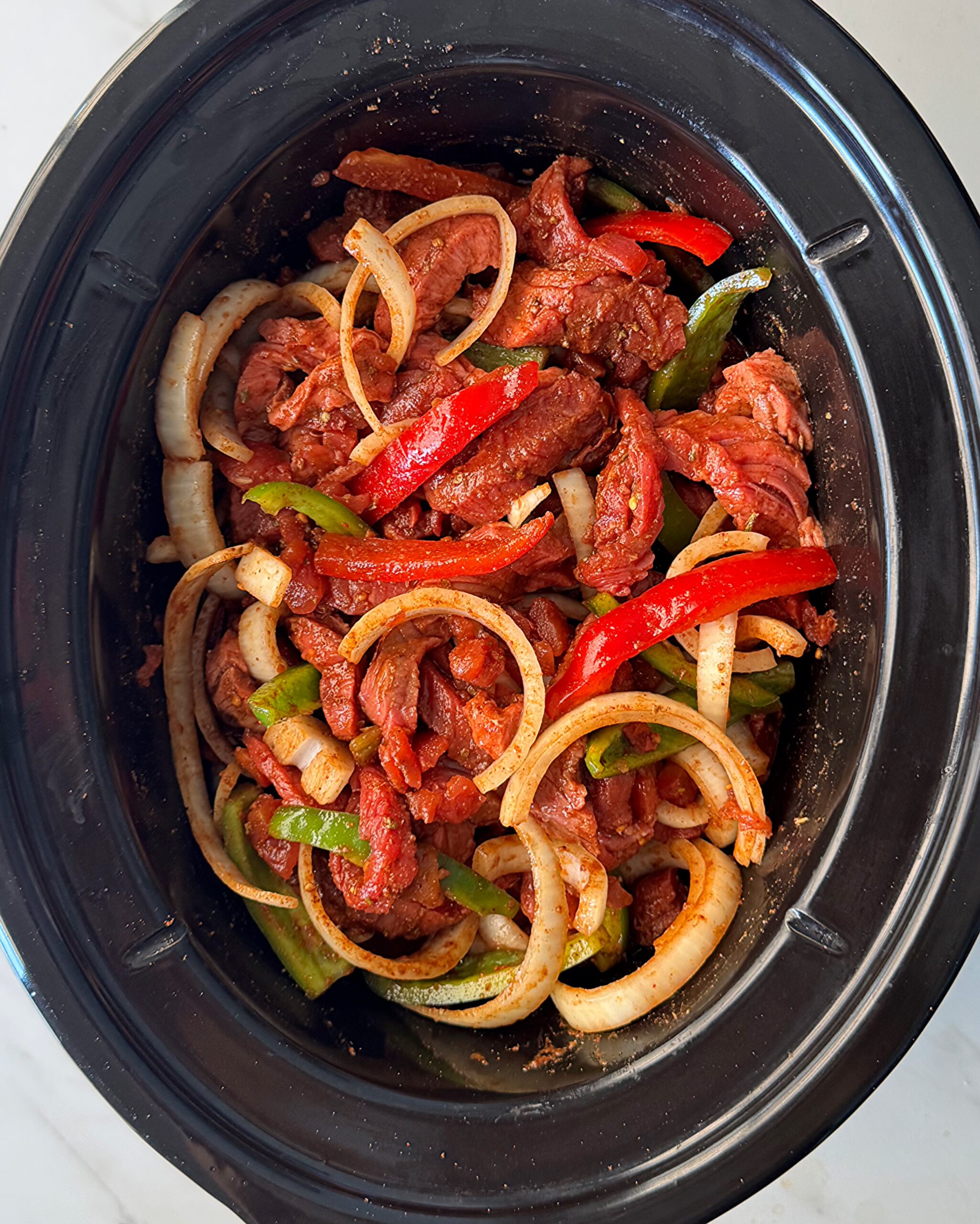 overhead shot of uncooked steak fajitas in a black slow cooker