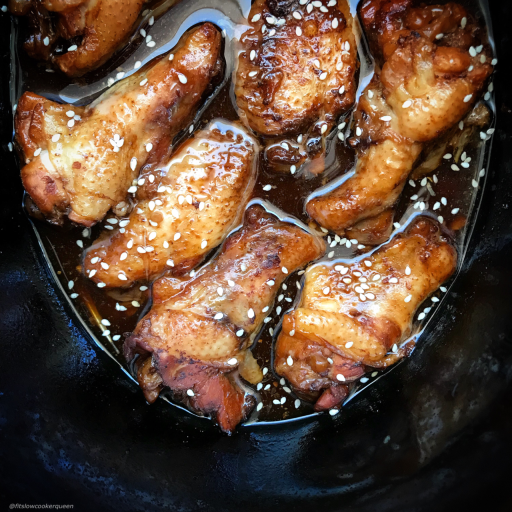 overhead shot of teriyaki chicken wings in a black slow cooker garnished with sesame seeds