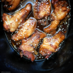 overhead shot of teriyaki chicken wings in a black slow cooker garnished with sesame seeds
