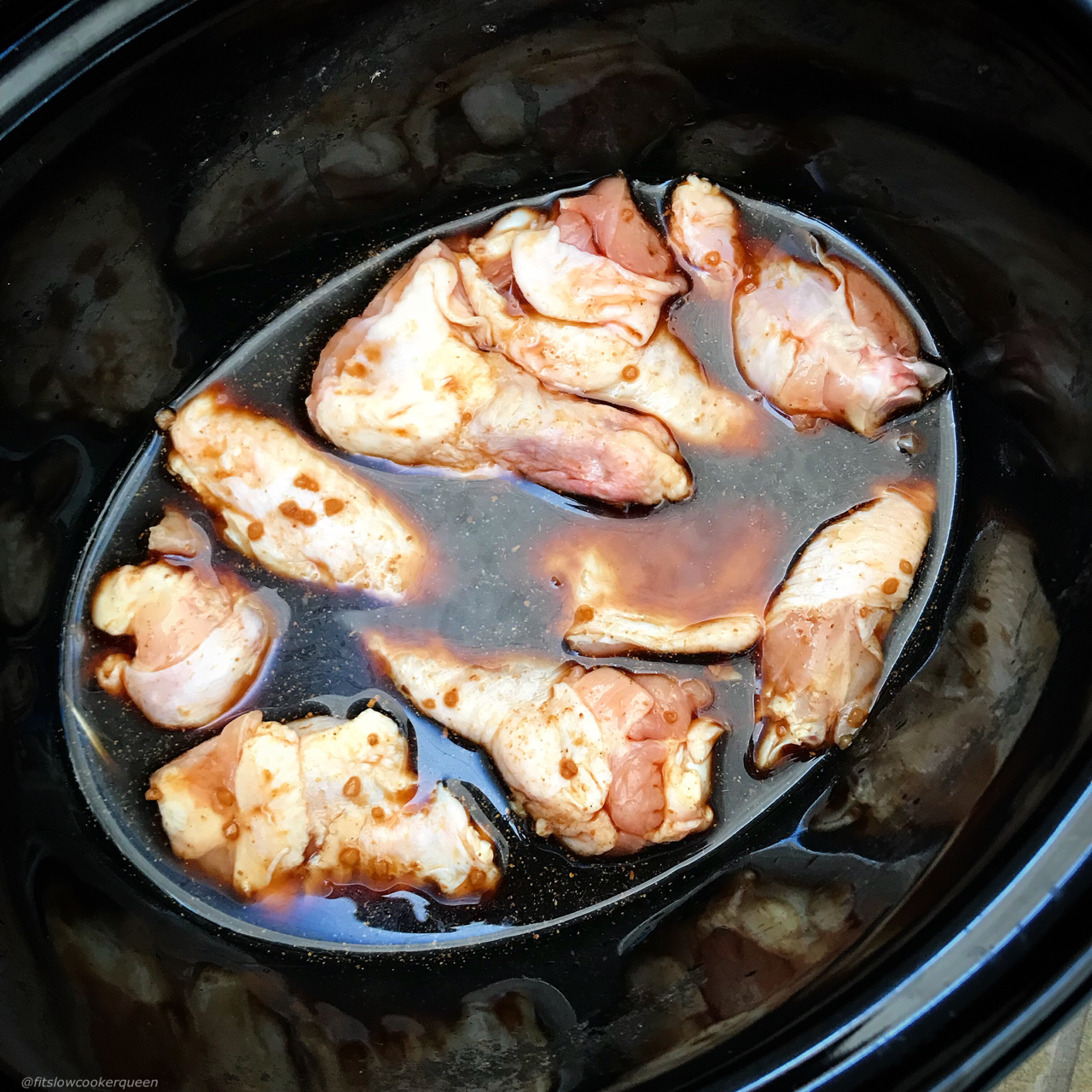 overhead before shot of uncooked teriyaki chicken wings in a black slow cooker