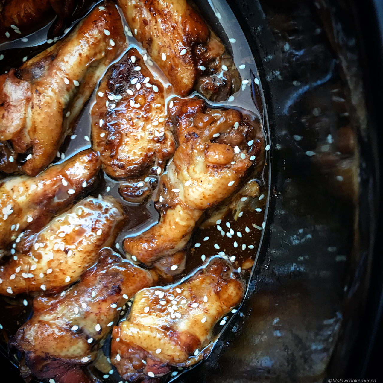 overhead shot of teriyaki chicken wings in a black slow cooker garnished with sesame seeds