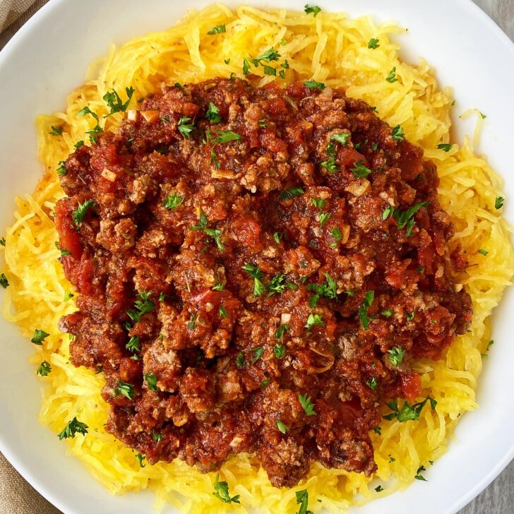 overhead shot of cooked spaghetti squash with meat sauce on top on a white plate