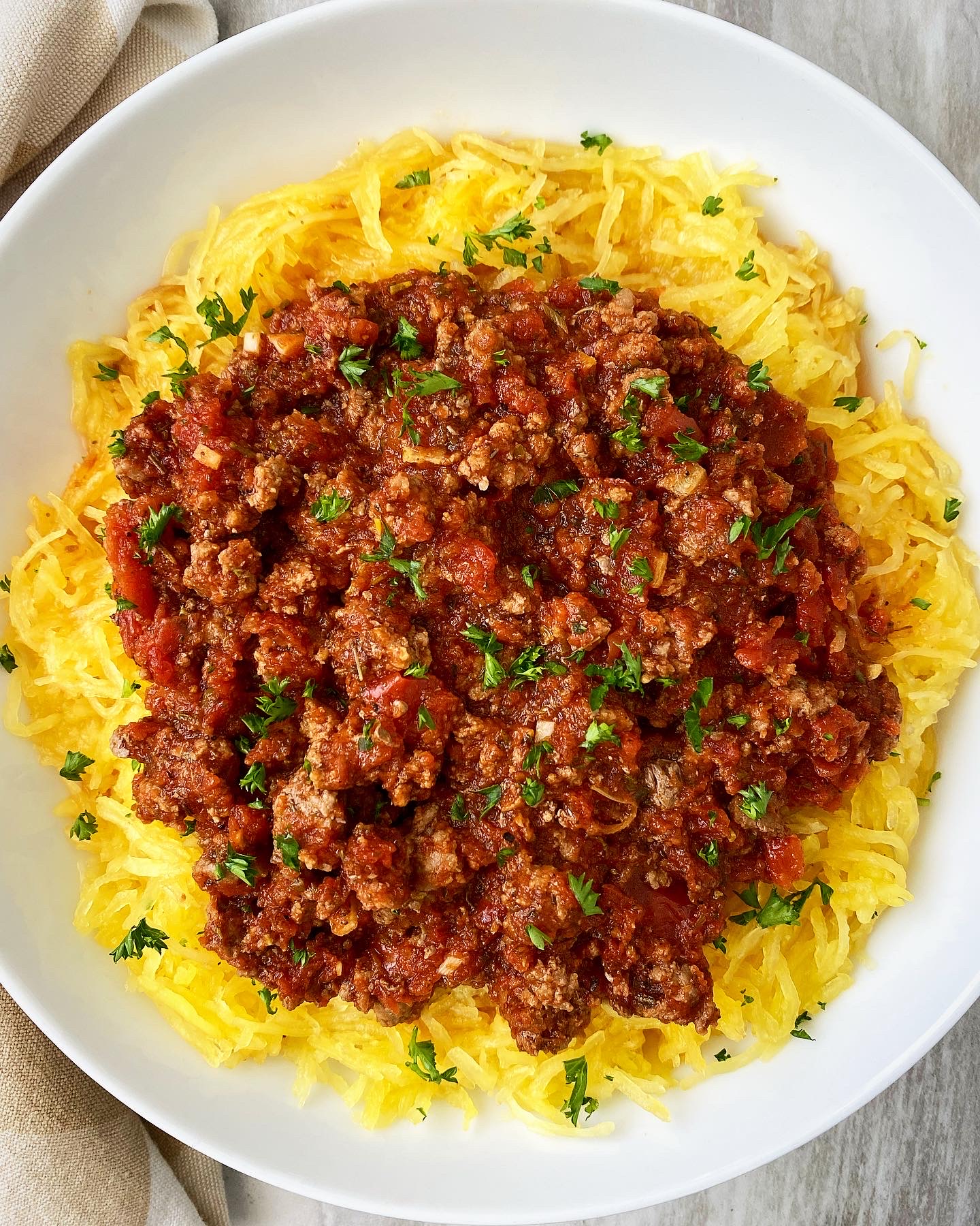 overhead shot of cooked spaghetti squash with meat sauce on top on a white plate