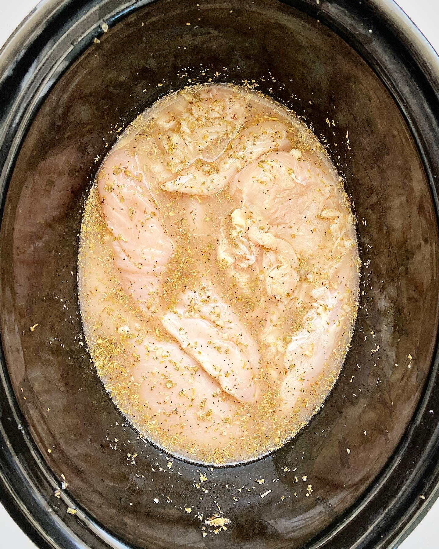 overhead shot of uncooked Greek chicken in the slow cooker