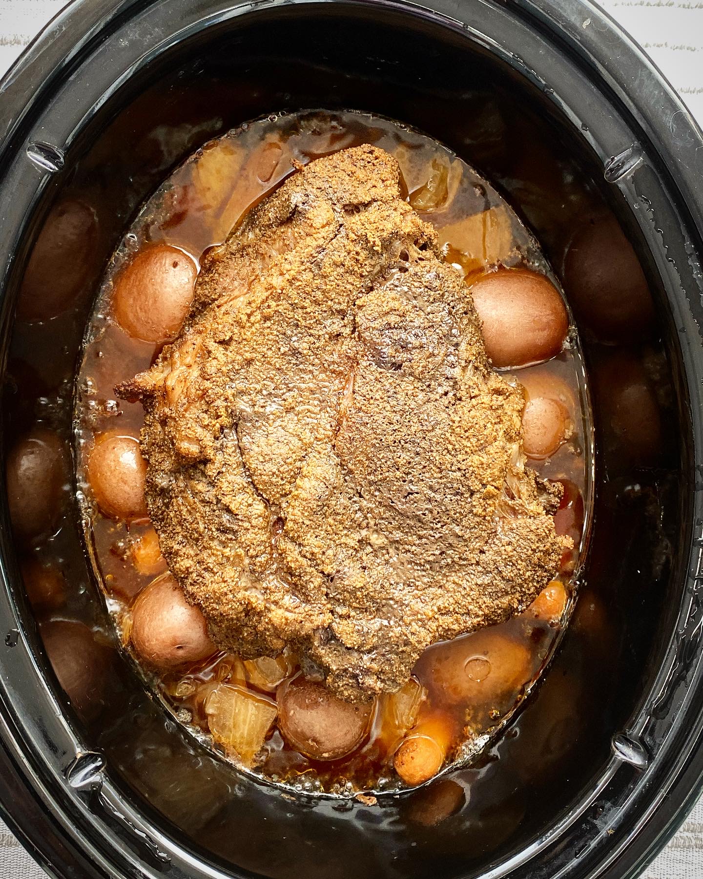 overhead shot of of cooked crockpot cumin beef pot roast in a black slow cooker