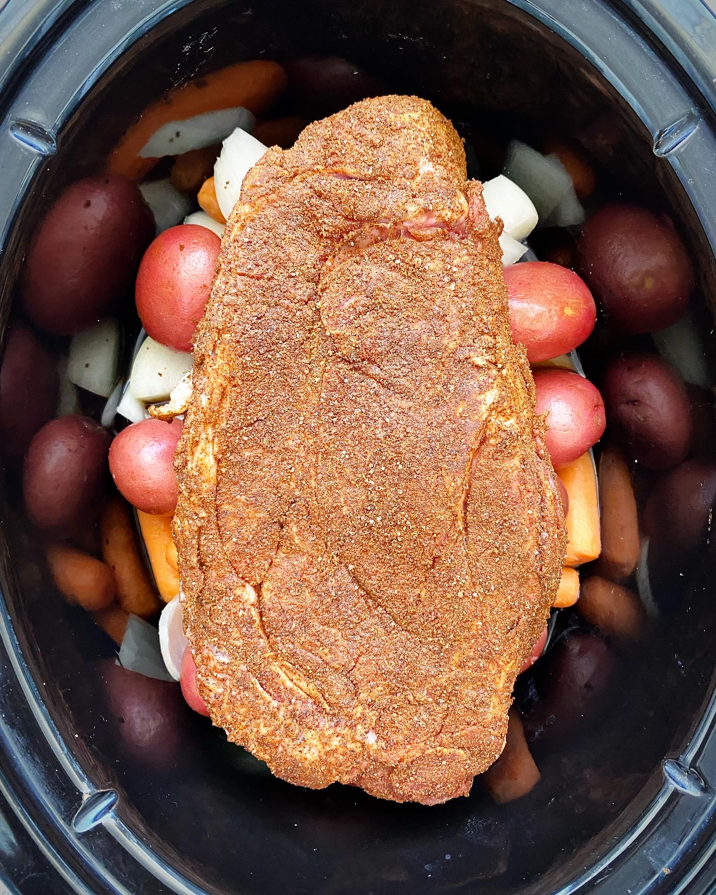 overhead shot of of cooked crockpot cumin beef pot roast in a black slow cooker