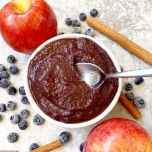pic of blueberry applesauce in a bowl surrounded by apples, blueberries, and cinnamon sticks