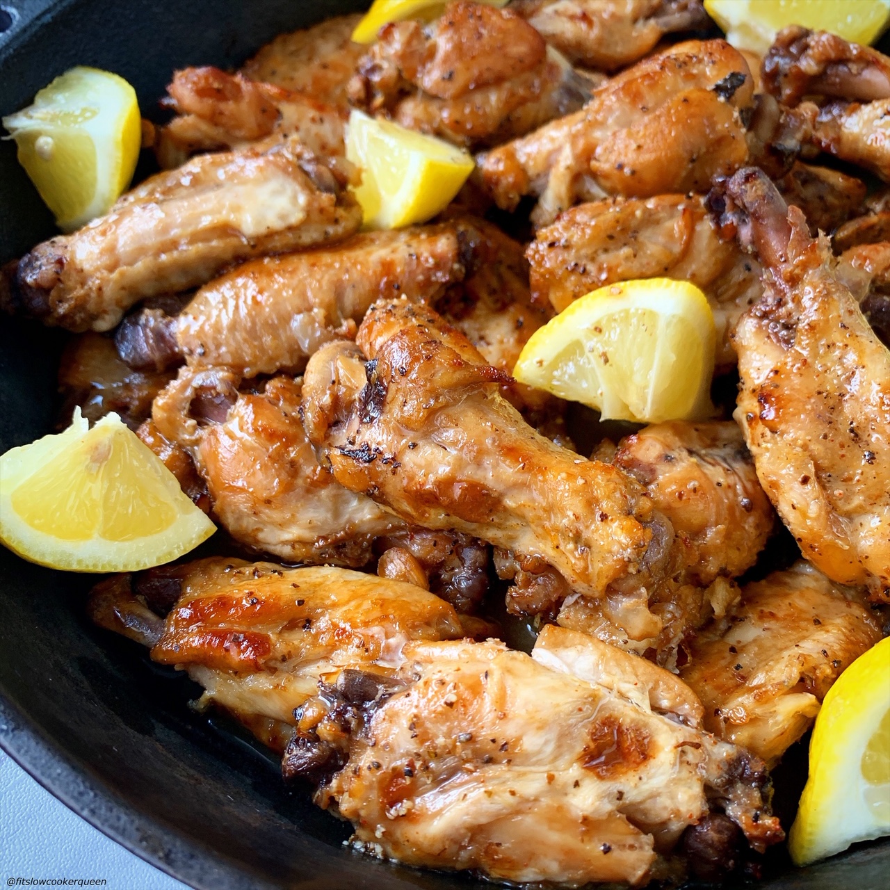 overhead shot of lemon pepper chicken wings in a black pan garnished with lemon wedges