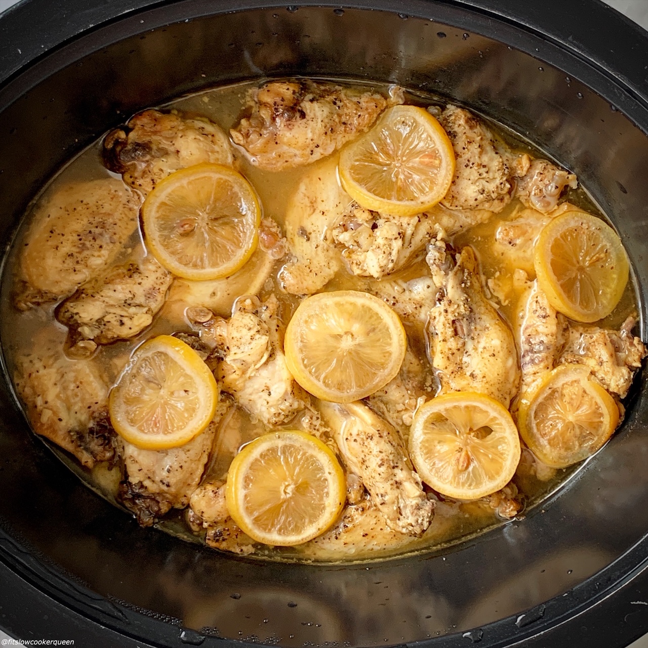 overhead shot of cooked lemon pepper chicken wings in a black slow cooker