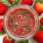 overhead shot of Strawberry Basil Jam on a mason jar surrounded by strawberries
