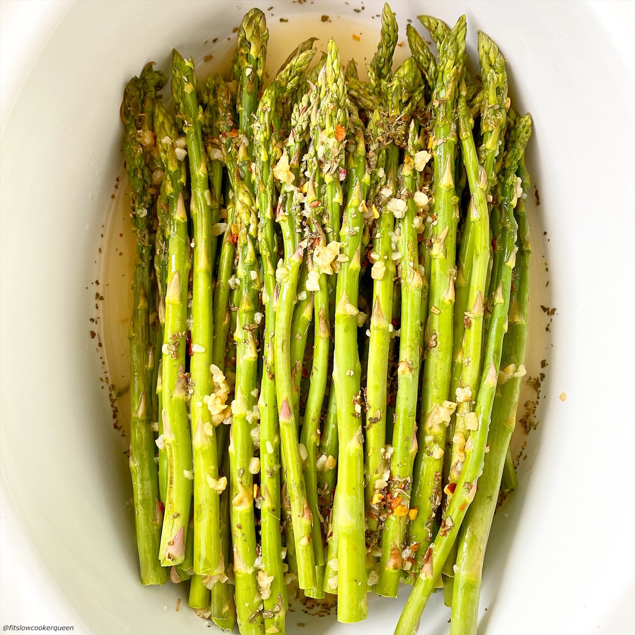 close up of raw asparagus in a bowl topped with seasonings and garlic