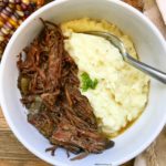 overhead shot of shredded beef in a white bowl with mashed potatoes