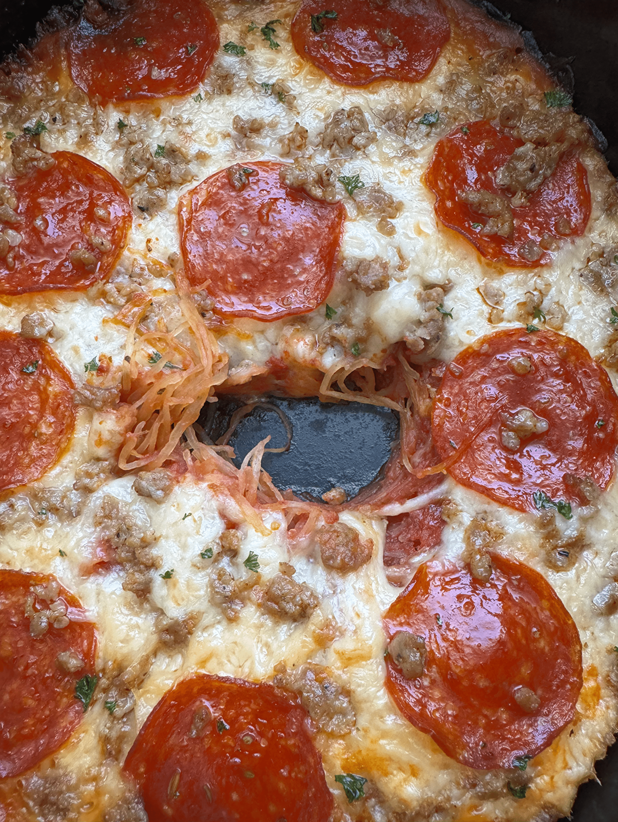 close up shot of cooked spaghetti squash pizza with pepperoni and sausage with a hole missing