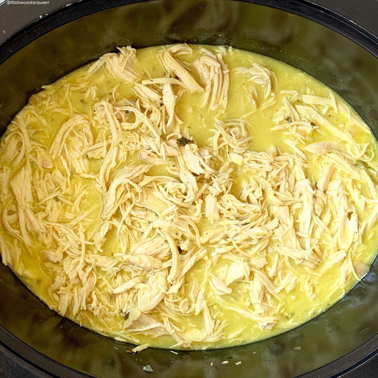 overhead shot of cooked, shredded chicken in a black slow cooker
