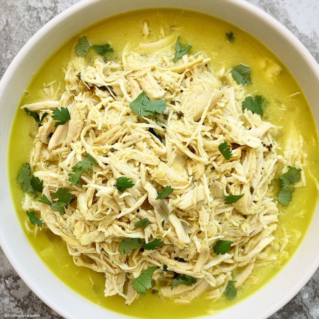 overhead shot of cooked, shredded chicken in a a white bowl garnished with fresh cilantro