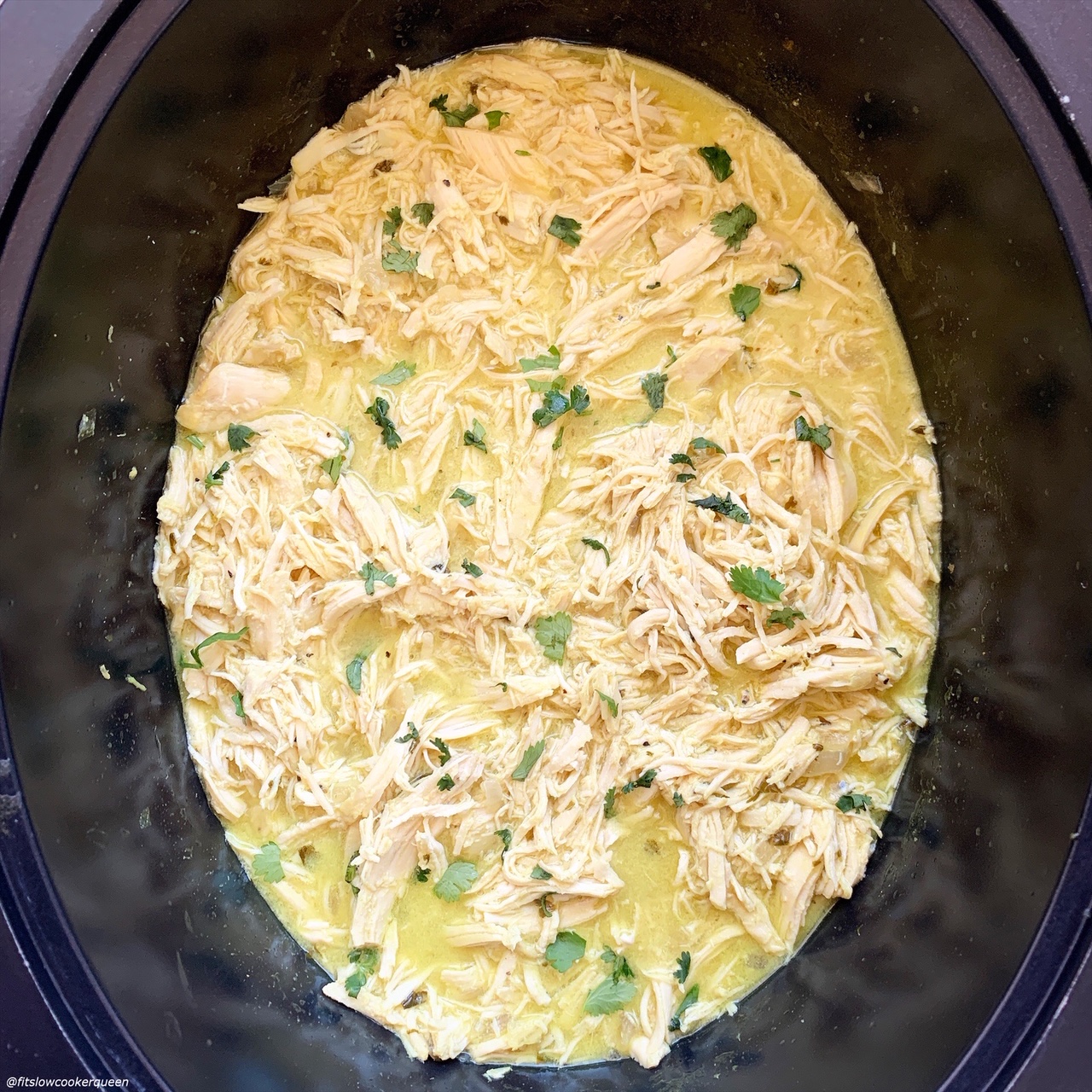 overhead shot of cooked, shredded chicken in a black slow cooker