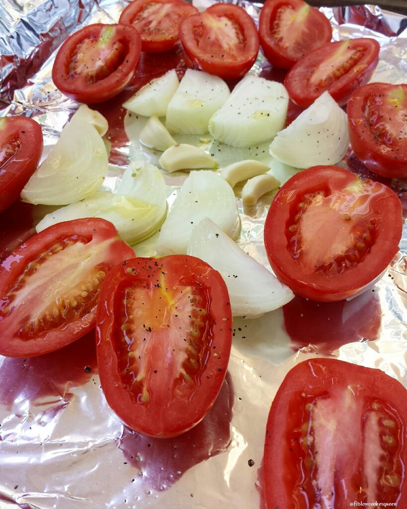 uncooked tomatoes, onion, and garlic on a lined baking sheet