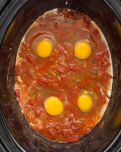 overhead shot of cooked slow cooker shakshuka in a black slow cooker with raw eggs added