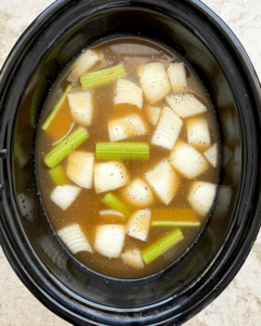 overhead shot of uncooked Crockpot Copycat Benihana Chicken Onion Soup in a black slow cooker