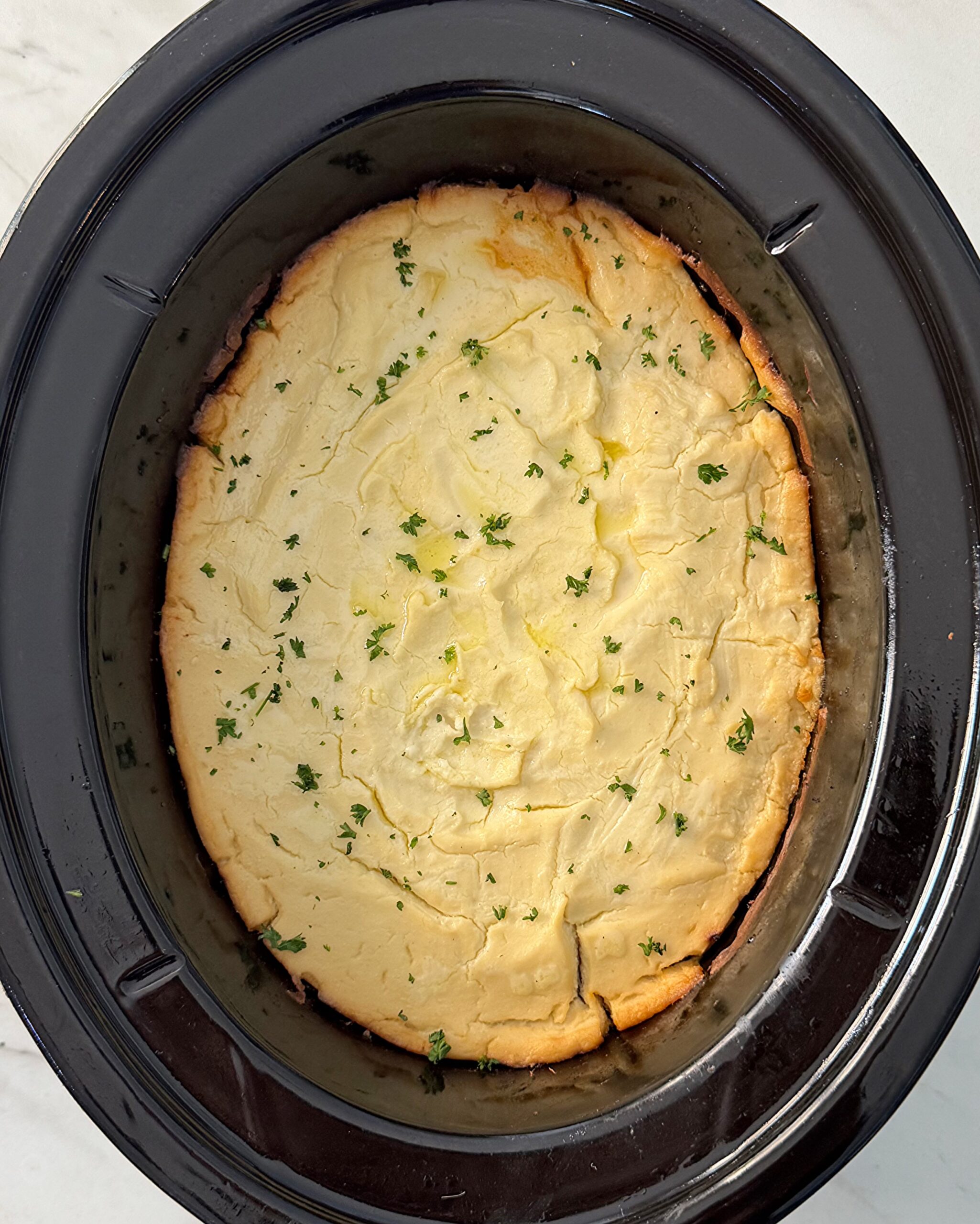 overhead shot of cooked shepherd's pie in a black slow cooker with mashed cauliflower topping