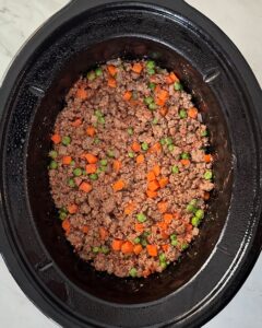 overhead shot of uncooked shepherd's pie in a black slow cooker