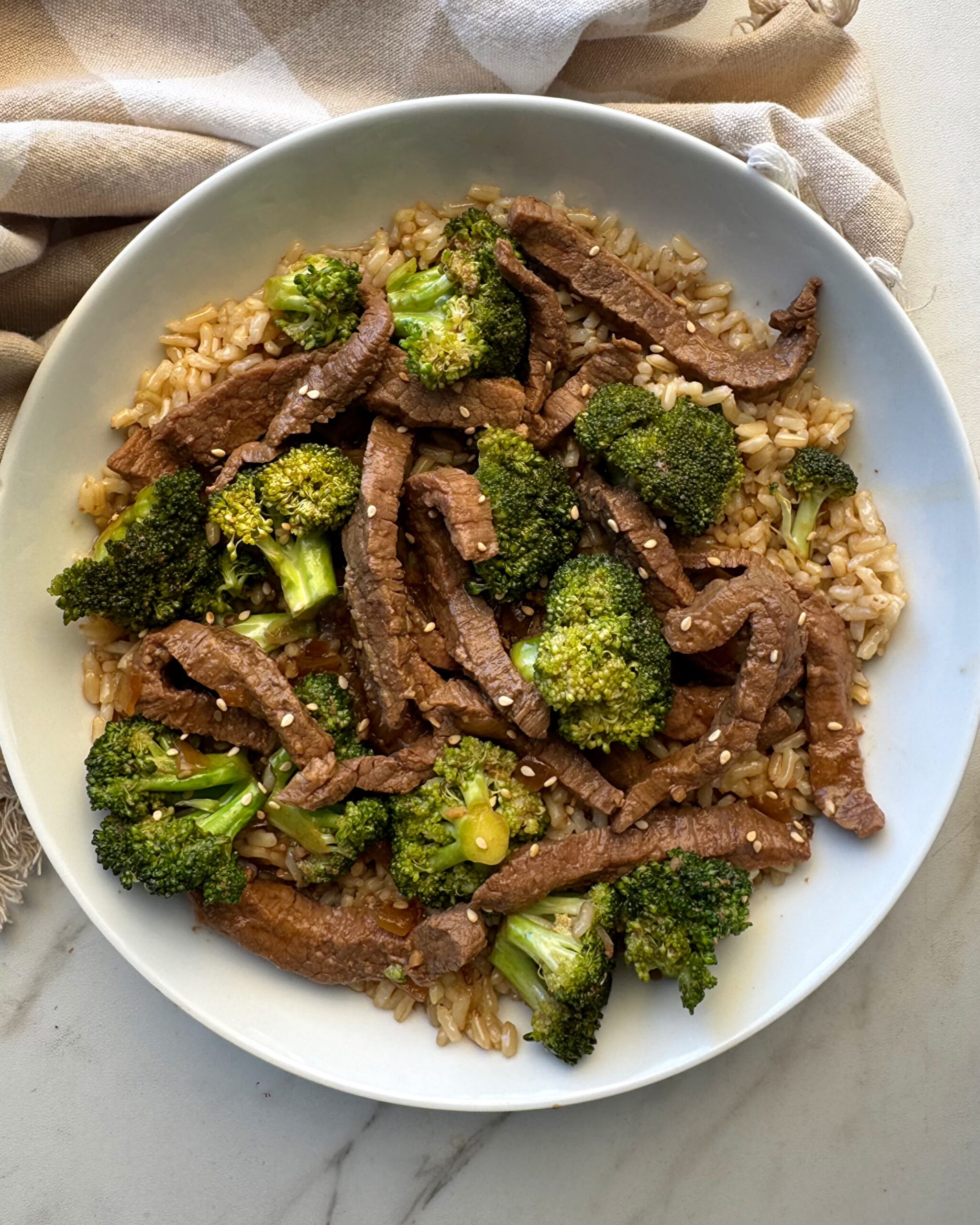 overhead shot of beef and broccoli in a white bowl served over brown rice