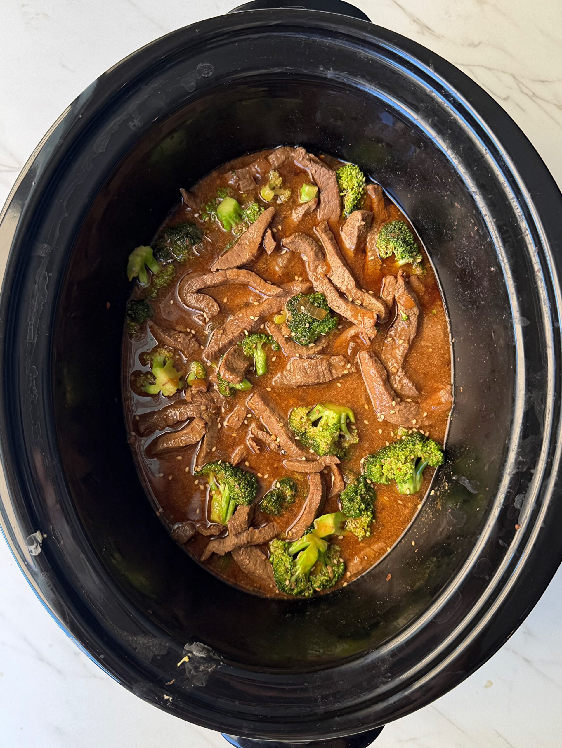 overhead shot of cooked beef and broccoli in a black slow cookerafter