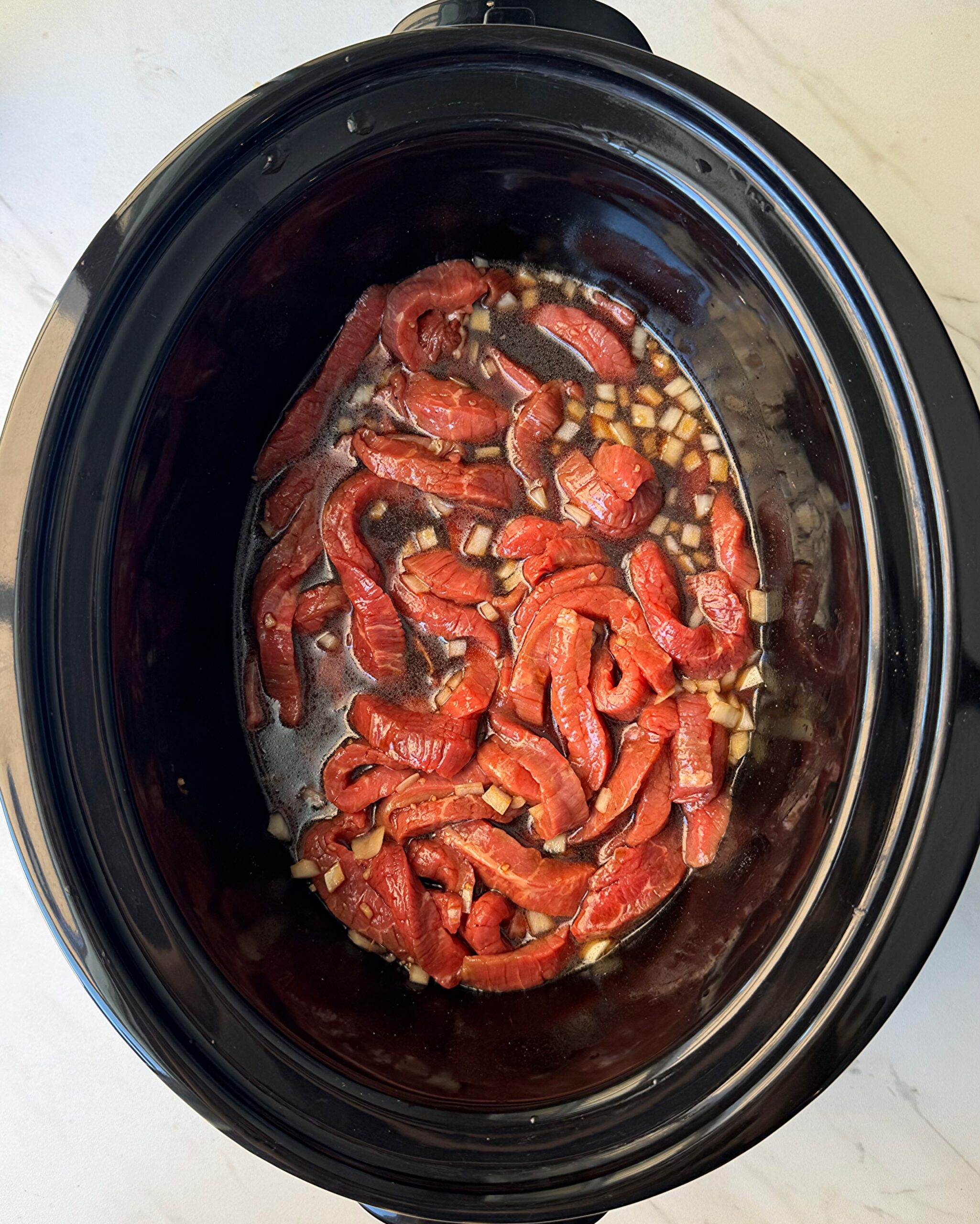 overhead shot of uncooked beef and broccoli in a black slow cooker