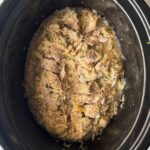 overhead shot of cooked Pork and Sauerkraut in a black slow cooker garnished with fresh parsley
