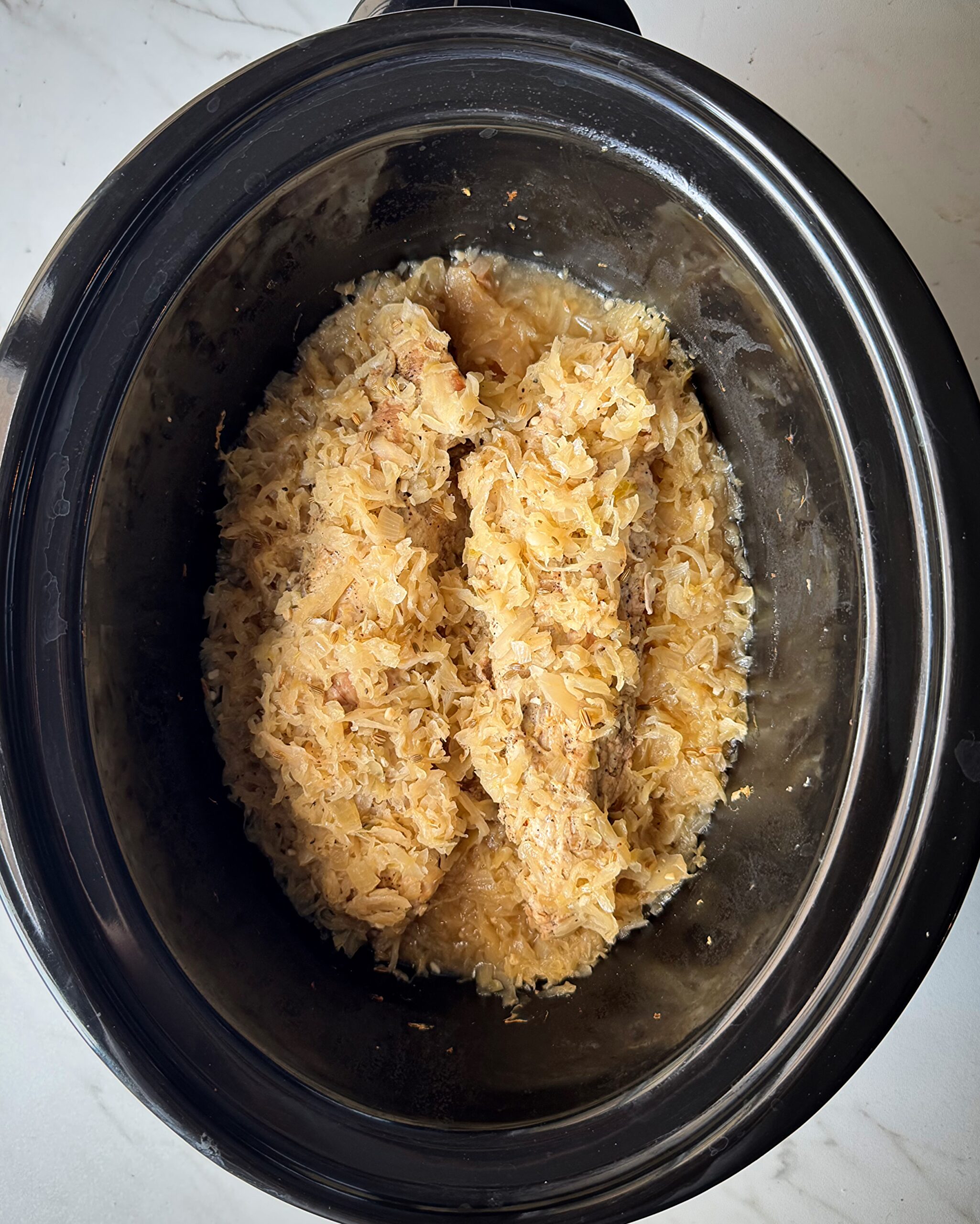 overhead shot of cooked Pork and Sauerkraut in a black slow cooker