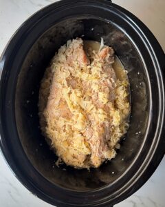 overhead shot of uncooked Pork and Sauerkraut in a black slow cooker