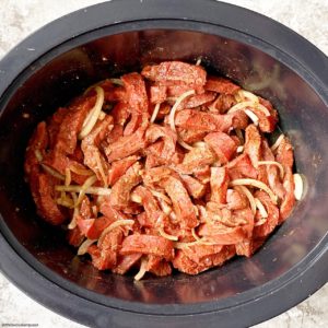 overhead shot of uncooked beef shawarma in a black slow cooker