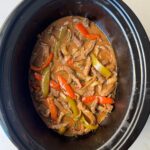 overhead shot of cooked pepper steak in a black slow cooker