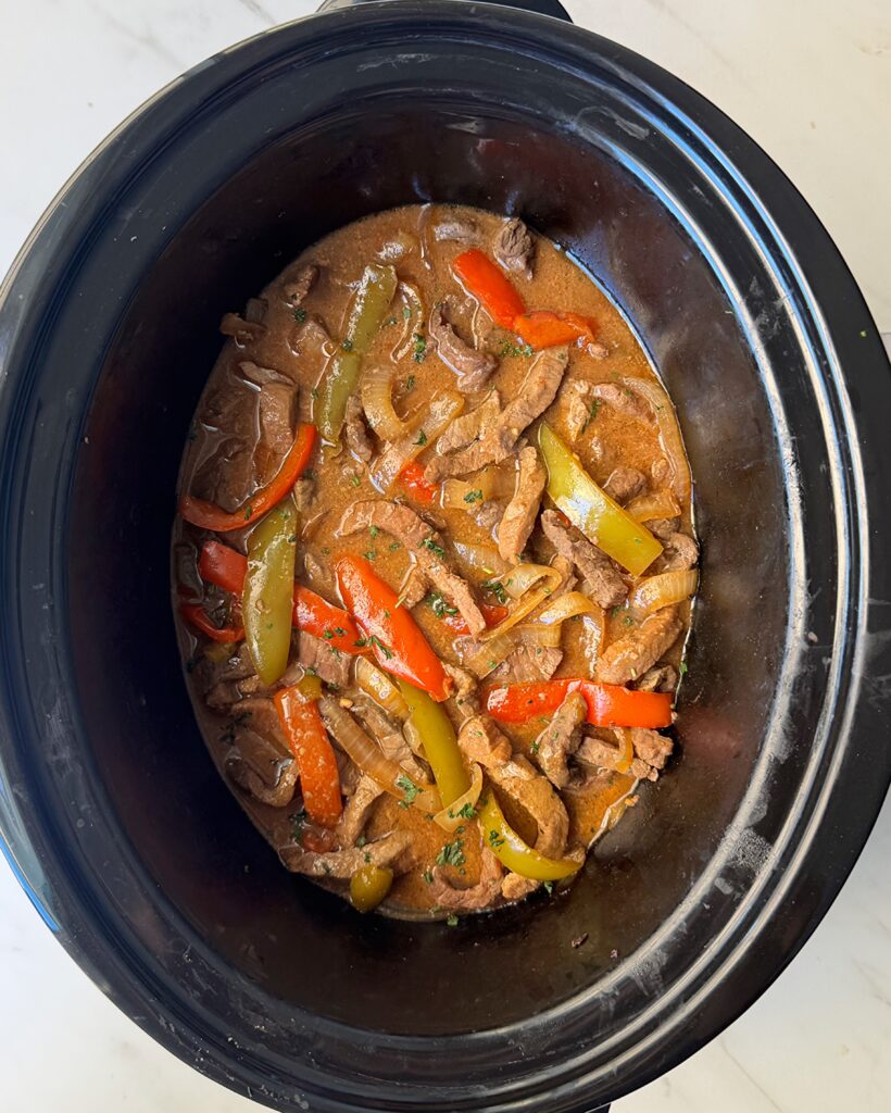 overhead shot of cooked pepper steak in a black slow cooker