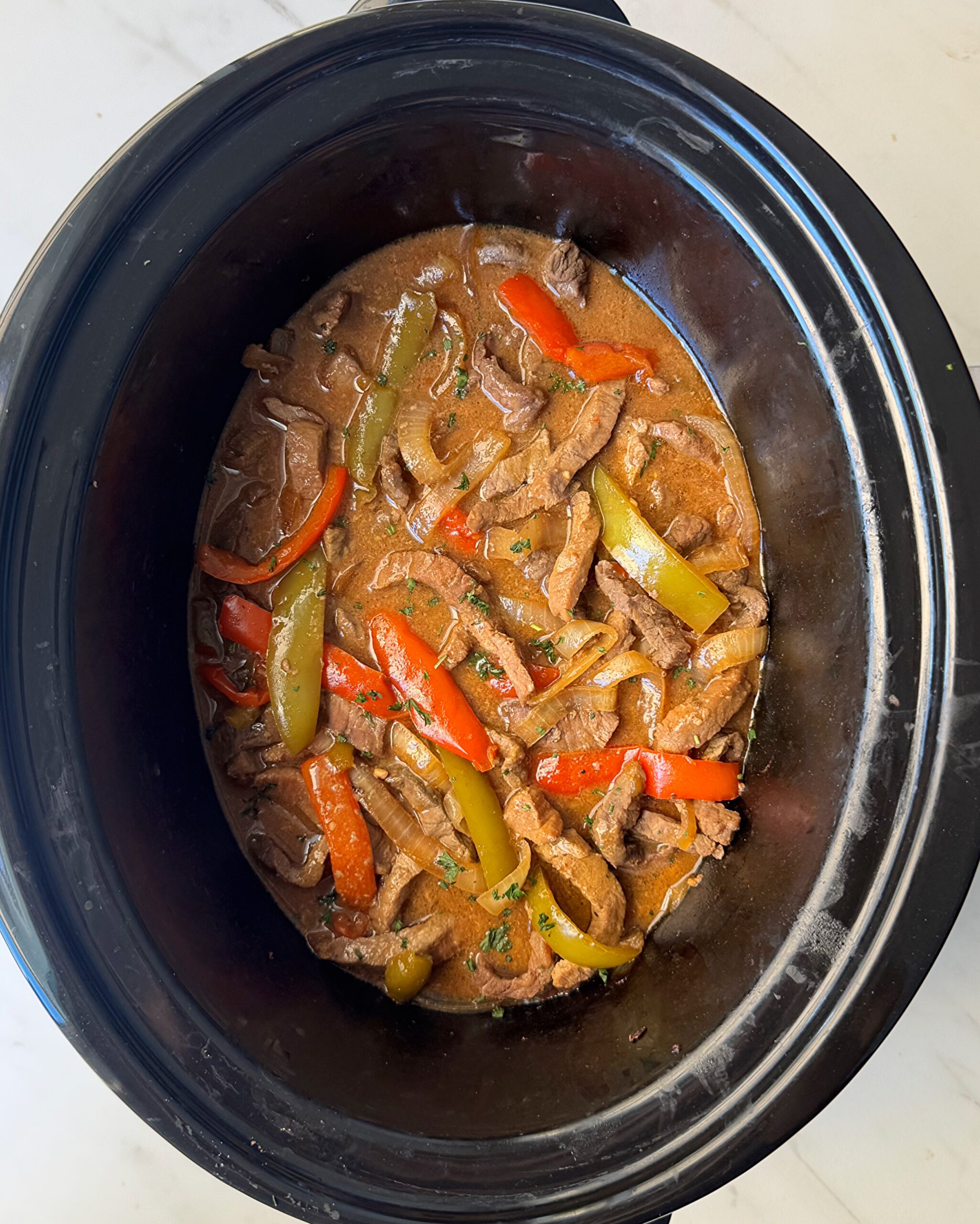 overhead shot of cooked pepper steak in a black slow cooker