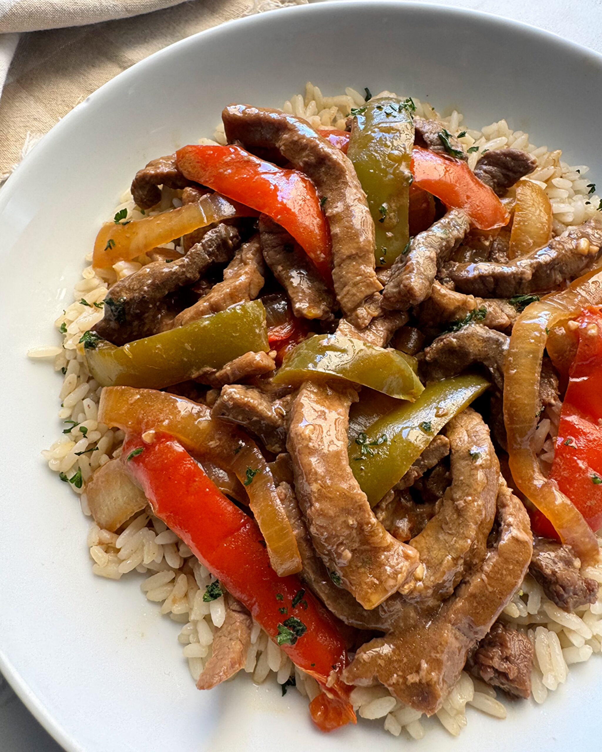 close up shot of slow cooker pepper steak on a white plate over white rice