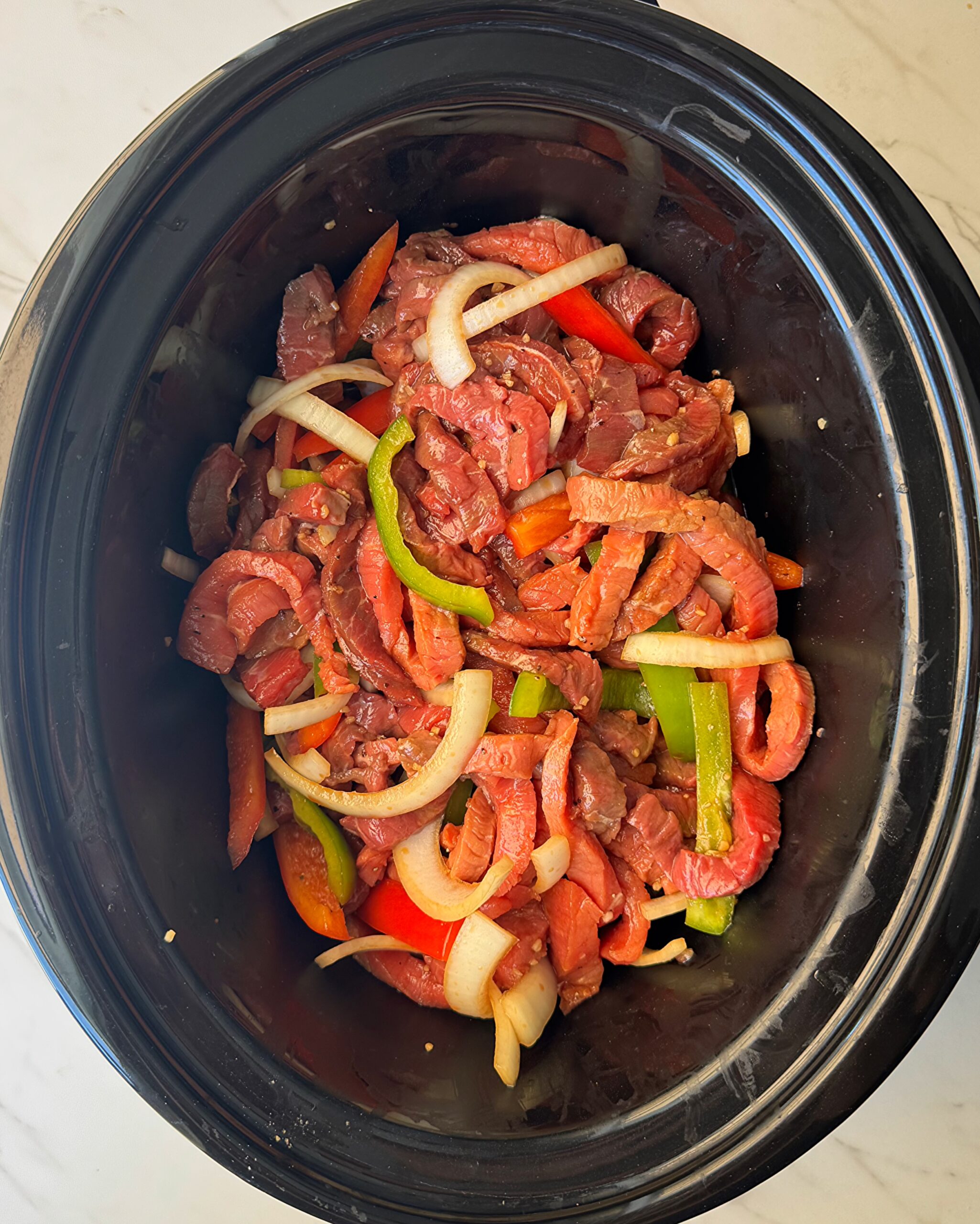 overhead shot of uncooked pepper steak in a black slow cooker