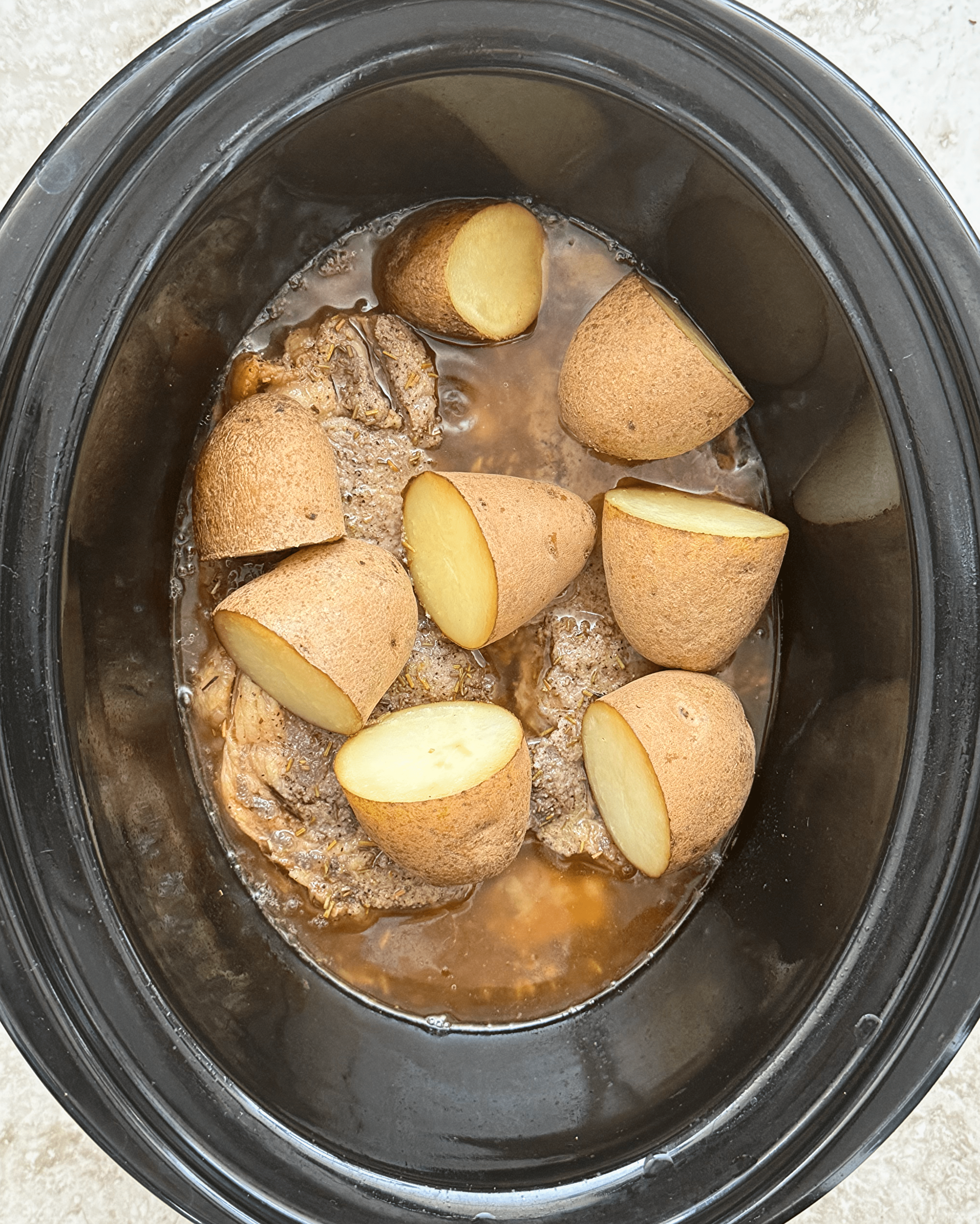 over head shot of cooked steak and potatoes in a black slow cooker