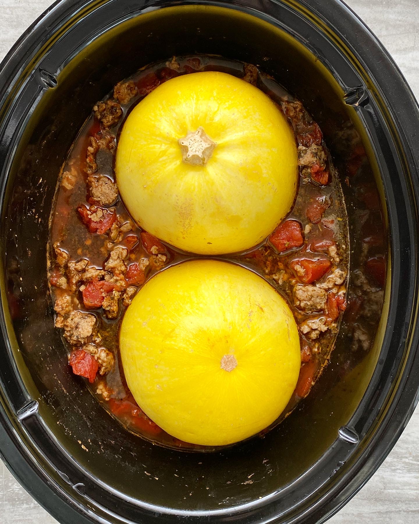overhead shot of cooked spaghetti squash, meat, tomatoes in a black slow cooker