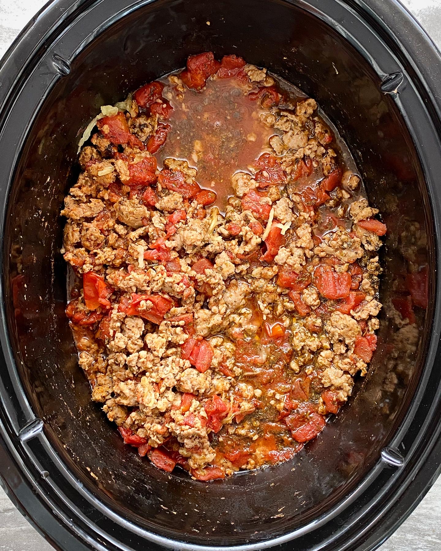 overhead shot of cooked meat & tomatoes in a black slow cooker