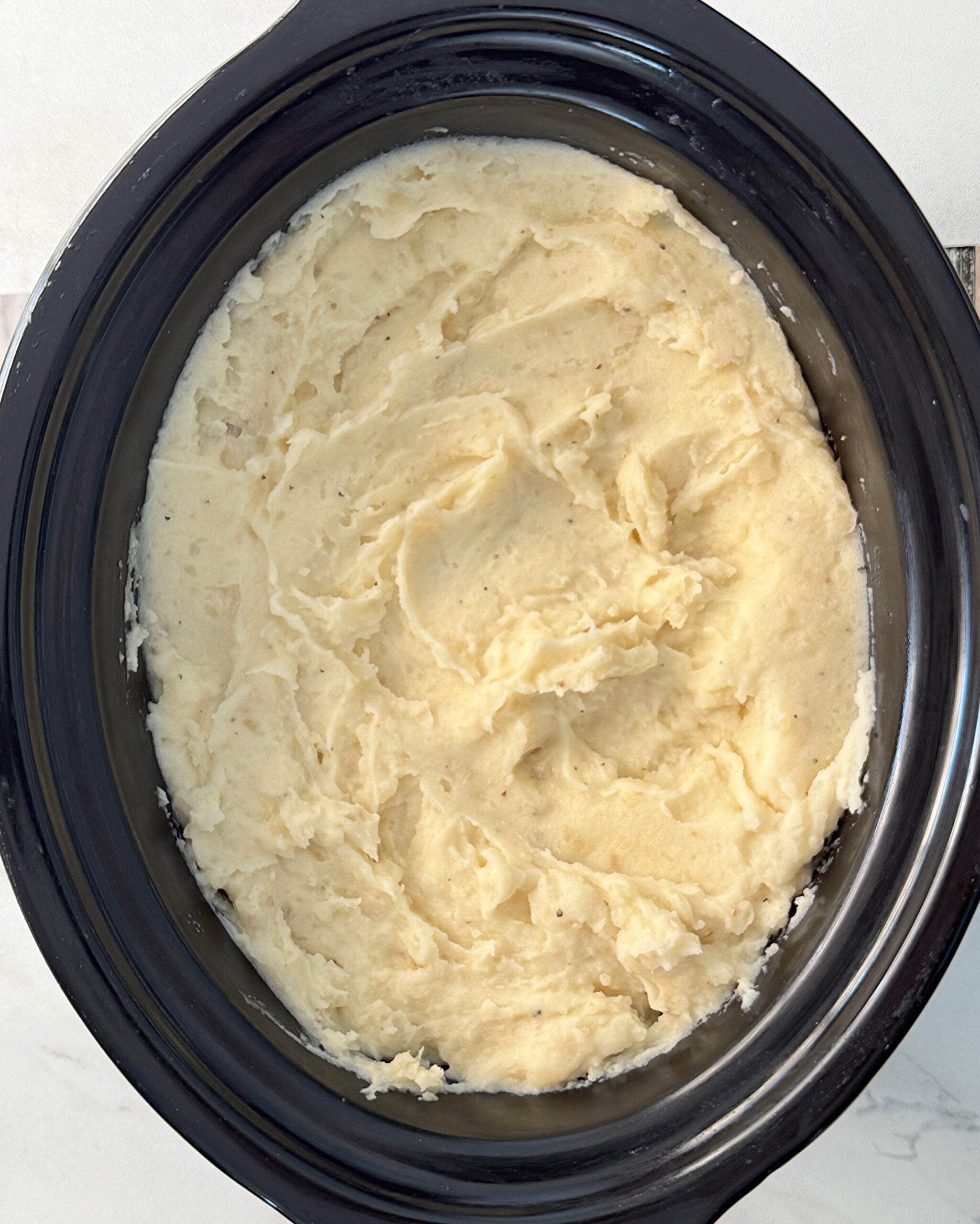 overhead shot of cooked mashed Potatoes in a black slow cooker 