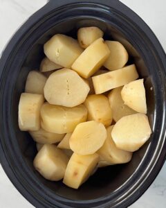 overhead shot of cooked un-mashed Potatoes in a black slow cooker