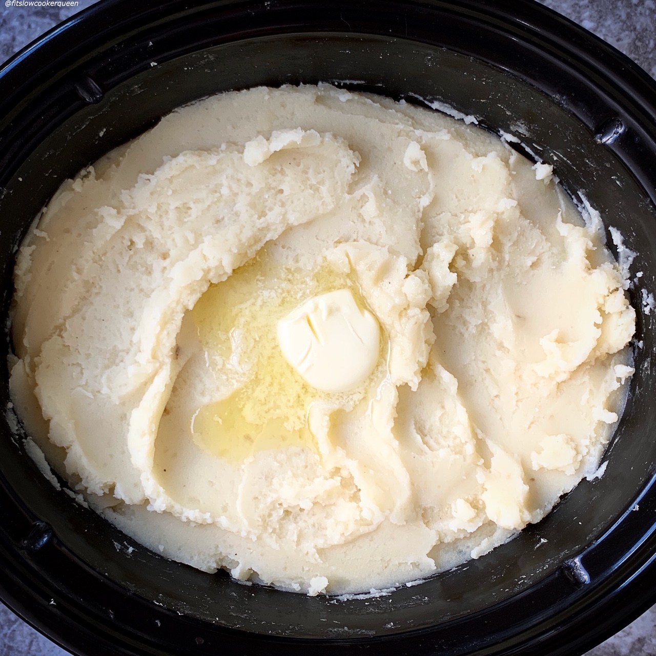 cooked potatoes in the slow cooker that have been mashed with a tablespoon of butter on top