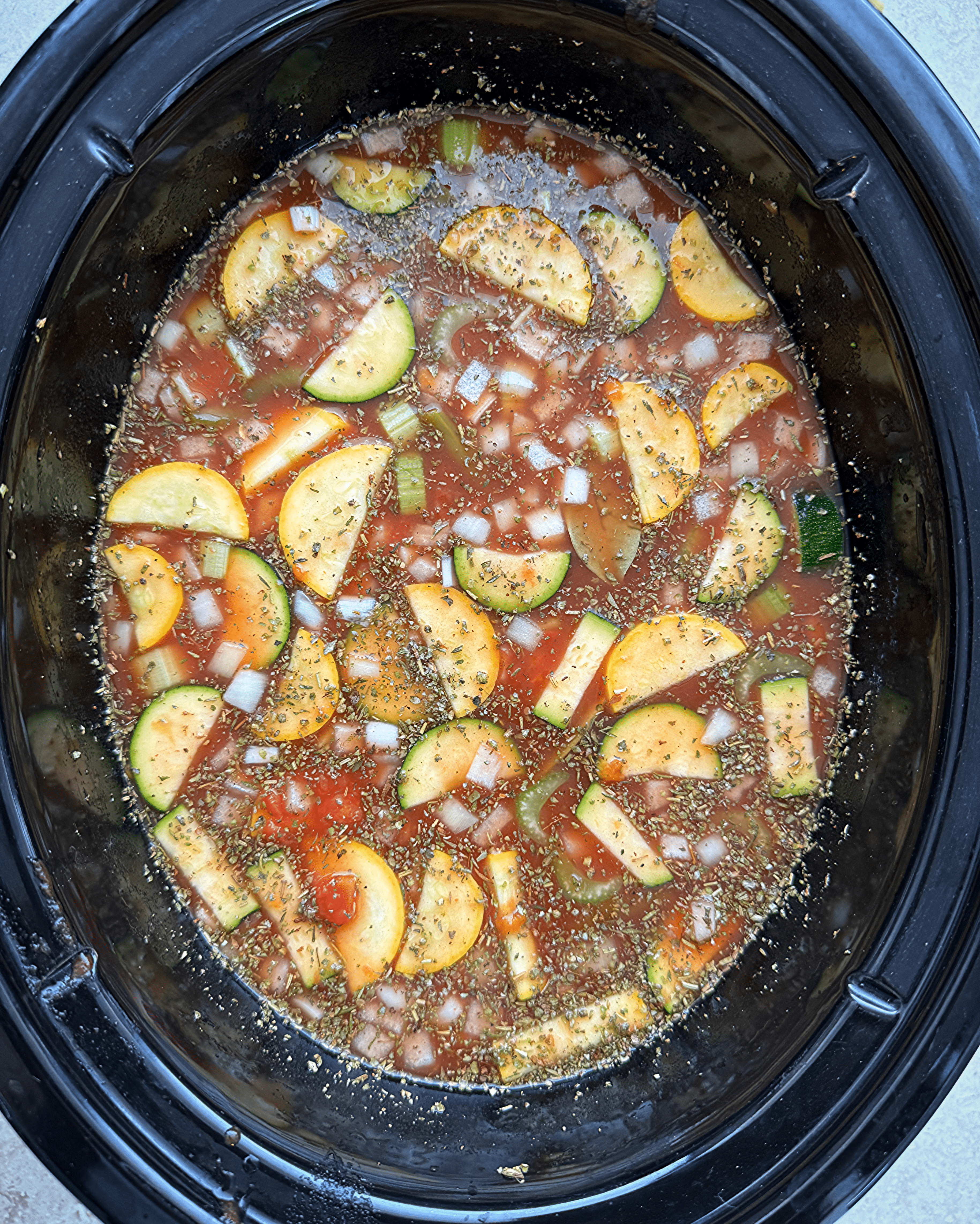 overhead shot of uncooked minestrone soup in a black slow cooker